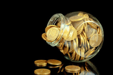 Yellow coins in a glass jar on a black background with reflection.