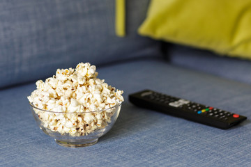 A glass bowl of popcorn and remote control. Evening cozy watching a movie or TV series at Home