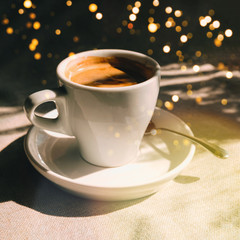 Cup of coffee on table in cafe with bright morning sunlight and with bokeh lights from the window
