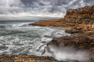 Fototapeta premium A long exposure under extreme clouds of wild waves that hit the rocky coast in Spain and swirl the water, which looks soft in the photo.