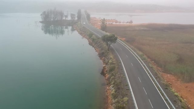 A Frontal Shot Of A White Car Coming Towards The Camera In By A Road Between Two Lakes