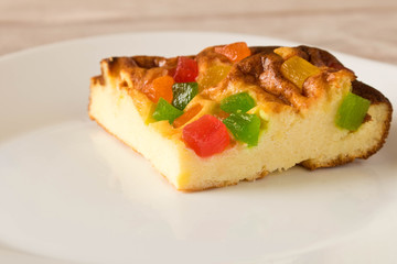 A piece of cottage cheese casserole with candied fruits on a white plate. Close up.