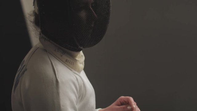 Close-up on a female fencers epee mask that pans down to her foil in slow motion