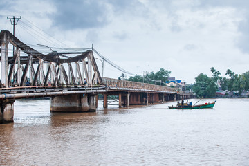 Khmer fishermen steering old fishing boat past under the ancient bridge.