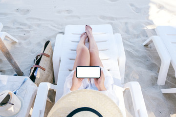 Top view image of a woman holding and using white mobile phone with blank desktop screen while...