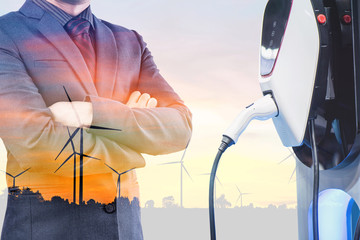 double exposure businessmen and silhouette of wind turbine at sunset with electric car battery...