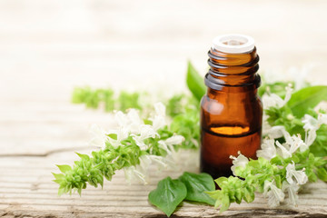 basil essential oil in the amber glass bottle, with fresh flowers, on the wooden board