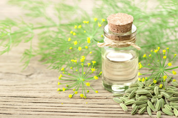 Obraz na płótnie Canvas fennel essential oil in the glass bottle, with seeds and flowers, on the wooden board