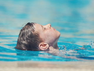 Cute European boy swimming backstroke in pool.