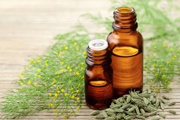 Fennel essential oil in the amber bottle with fennel flowers on the wooden board - obrazy, fototapety, plakaty