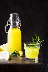 Traditional Italian lemon digestive liqueur in a glass served with a sprig of rosemary against dark background