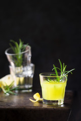 Traditional Italian lemon digestive liqueur in a glass served with a sprig of rosemary against dark background