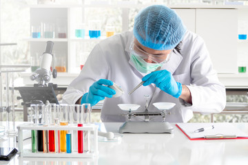 An Asian scientist or chemist using mechanical scale to gathering and measuring specimen  at laboratory. The young man wearing safety glasses in experiment. Pharmaceutical research concept.