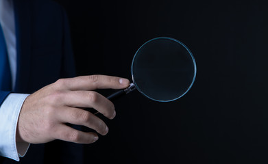 businessman in black background in the hands of a magnifier