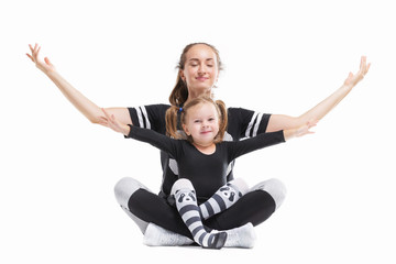 Portrait of healthy family of mother sitting in yoga pose with little daughter and raising hands isolated at white background.