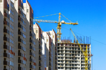 Finished Apartment Building and a New High-Rise Building Construction Site with Yellow Cranes against Blue Sky. Real Estate, Residential Buildings Urban Mixed-Use Development Concept.