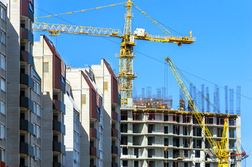 Finished Apartment Building and a New High-Rise Building Construction Site with Yellow Cranes against Blue Sky. Real Estate, Residential Buildings Urban Mixed-Use Development Concept.