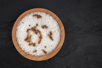 A bowl of sea salt infused with truffle shavings, shot from the top on a black background with a place for text