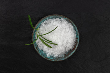 A bowl of rosemary infused sea salt, shot from the top on a black background with copy space