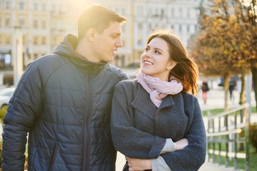 Outdoor portrait of happy embracing couple, handsome man and woman walking, background evening city