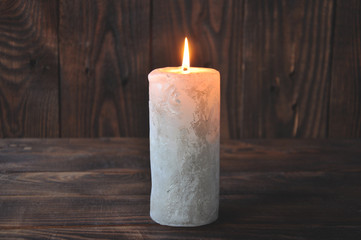 a large candle burns in the darkness on a wooden texture background