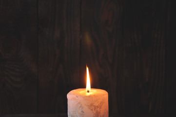a large candle burns in the darkness on a wooden texture background