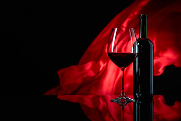 Wineglass and bottle of red wine on a black reflective background.