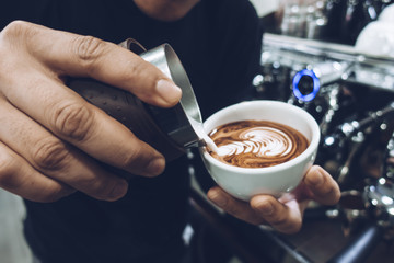Barista's hand pouring milk to make latte art on cappuccino coffee