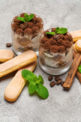 Classic tiramisu dessert in a glass and savoiardi cookies on concrete background