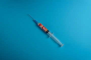 Syringe filled with colorful nano balls on a blue background. Innovative medical concept.