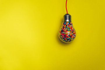 Lightbulb filled with multi colored ball on a yellow background behind. Best idea concept.