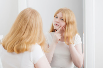 teen girl examines acne in front of mirror