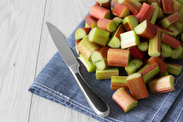 Pile of sliced rhubarb and knife on a blue tea towel with a grey wood background