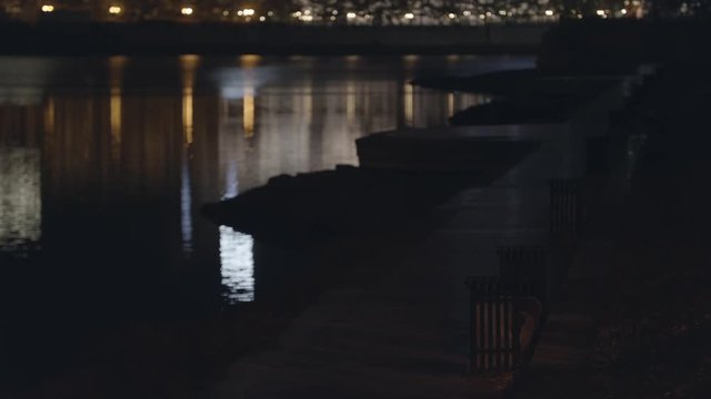 Empty asphalt sidewalk near the river, city at night. Stock footage. Beautiful night city landscape with embankment, benches near the river.