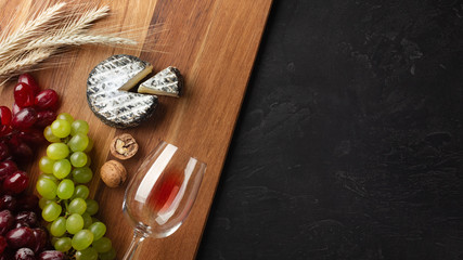 Cheese head, bunch of grapes, honey, nuts and wineglass on wooden board and black background