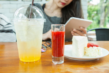 woman siting on wood table with smart pad in hand and strawbery crape cake ready to eat on table