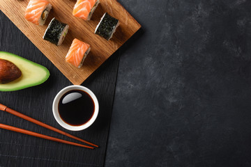 Set of sushi and maki rolls with sliced avocado on stone table