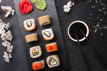 Fototapeta na wymiar Set of sushi and maki rolls with branch of white flowers on stone table