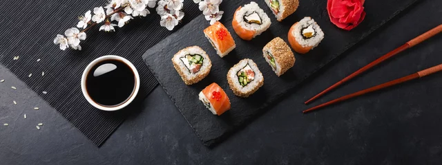 Fototapete Sushi-bar Satz Sushi und Maki-Rollen mit Zweig von weißen Blumen auf Steintisch