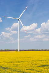 turbogenerator on a field of flowering canola, against a blue sky with clouds