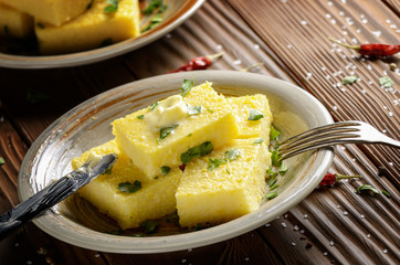 Polenta with butter and greens on clay dish on wooden rustic table