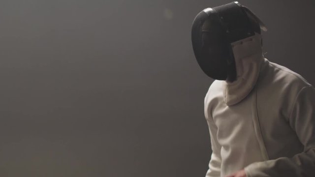 A male fencer adjusts his epee mask and prepares to duel with his sparring partner in slow motion