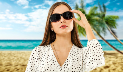 Slim young woman with sunglasses and beach landscape of palms. 