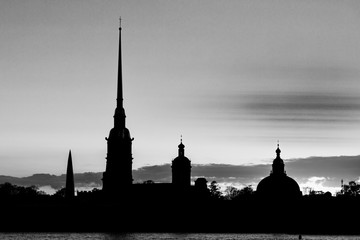 Naklejka premium The black and white silhouette of Peter and Paul Fortress in St. Petersburg, Russia in the rays of setting sun on the background of cloudy sky 