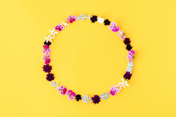 Flowers composition. Wreath made of purple, pink and white flowers on yellow background
