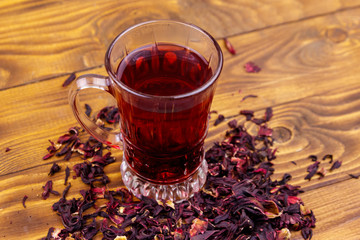 Glass cup of red hibiscus tea (carcade, roselle) on wooden table