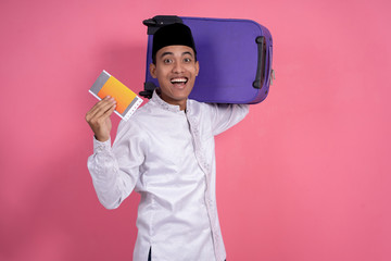 happy excited asian muslim male with islamic wear holding suitcase for eid mubarak holiday