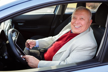 Old senior business man with tablet pc computer on driver seat looking to camera and smile with white teeth. Transport, business trip, technology and people concept