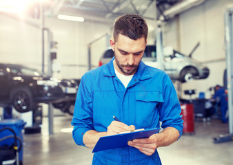 car service, repair, maintenance and people concept - auto mechanic man or smith with clipboard writing at workshop