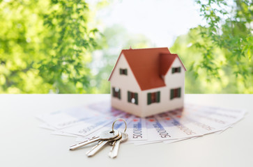 mortgage, real estate and property concept - close up of home model, money and house keys over...